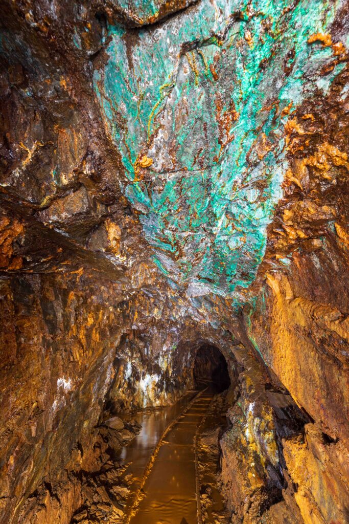 A rocky mine gallery with ochre walls and turquoise copper minerals on the ceiling