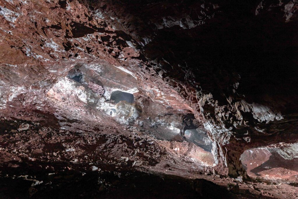 Vaste caverne minière aux roches rougeâtres éclairée artificiellement où se détache une petite silhouette