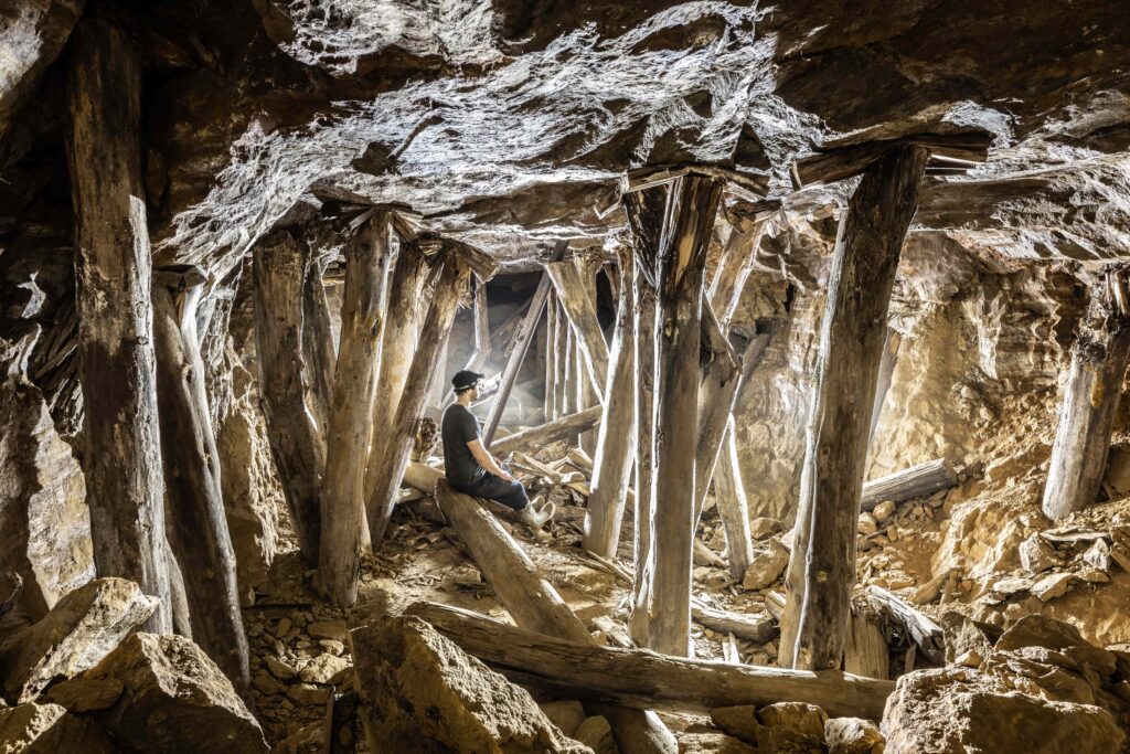 A man sitting among wooden timber supports inside an underground mine gallery