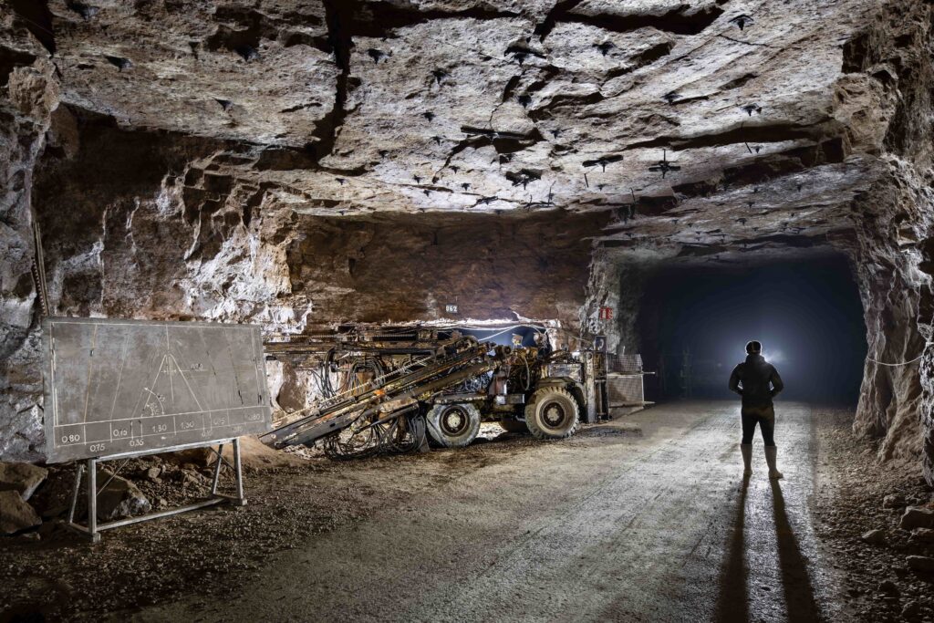 A person standing in an underground mine illuminates a drilling machine and a blackboard