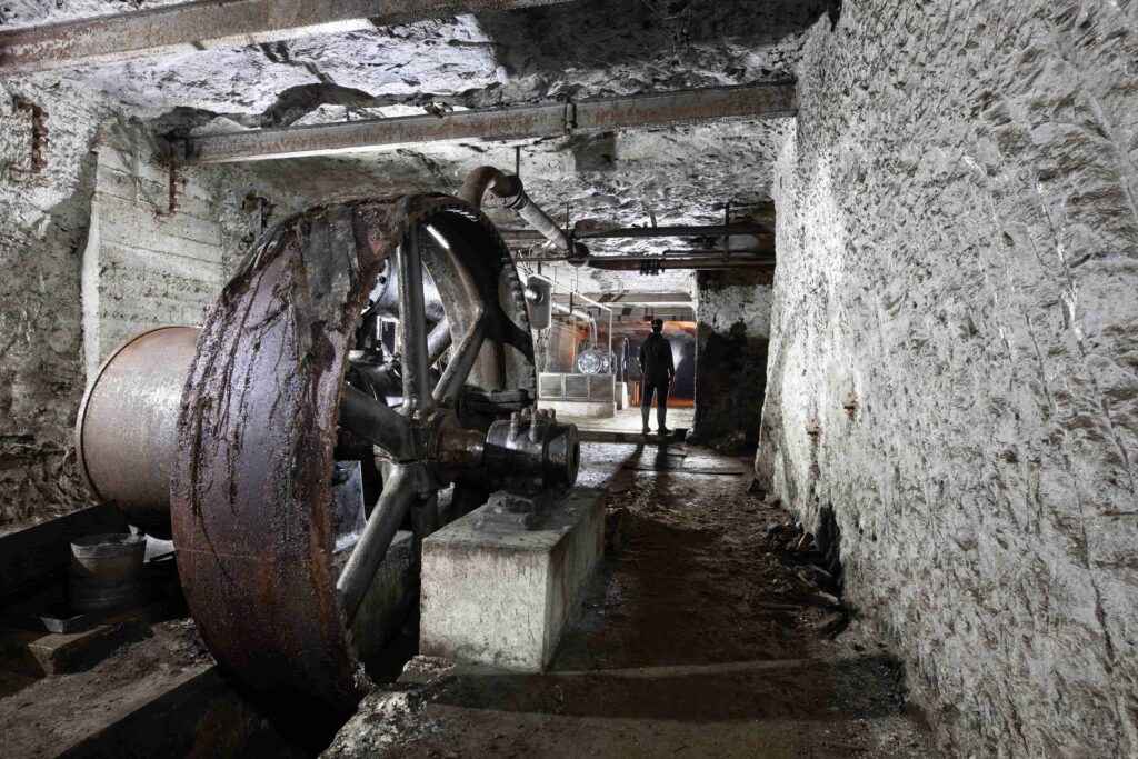 Large rusty metal compressor wheel in an underground gallery with a person in the background