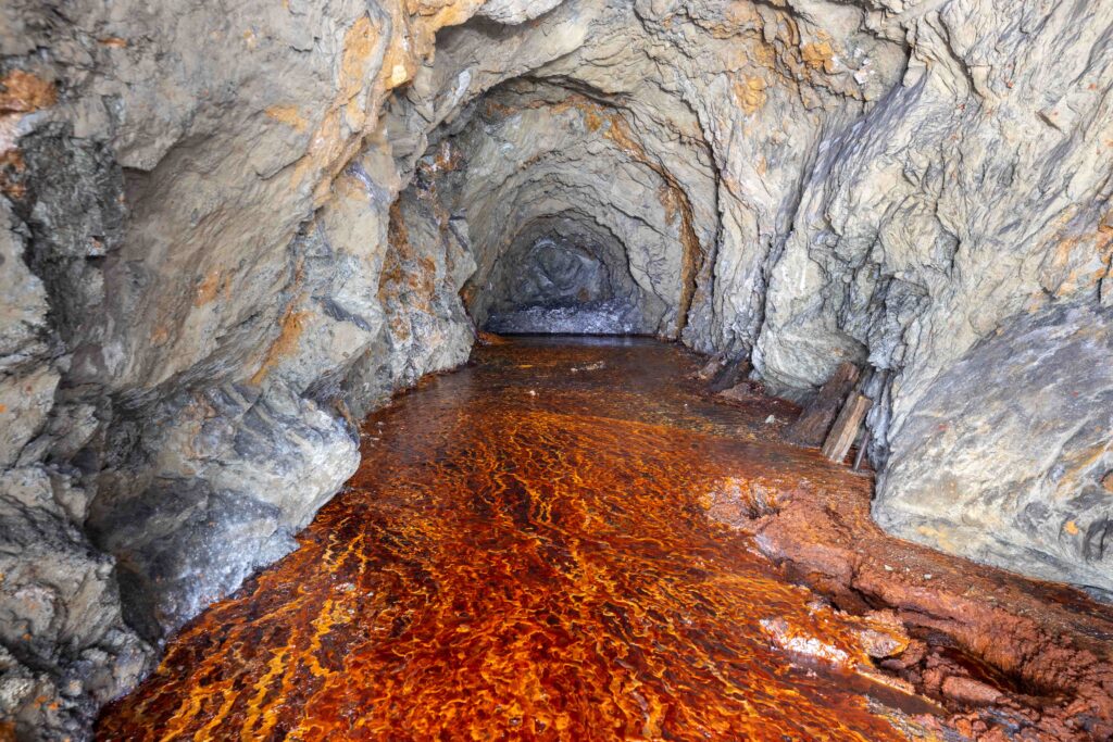 Un tunnel minier taillé dans la roche inondé d'une eau ocre aux teintes orange
