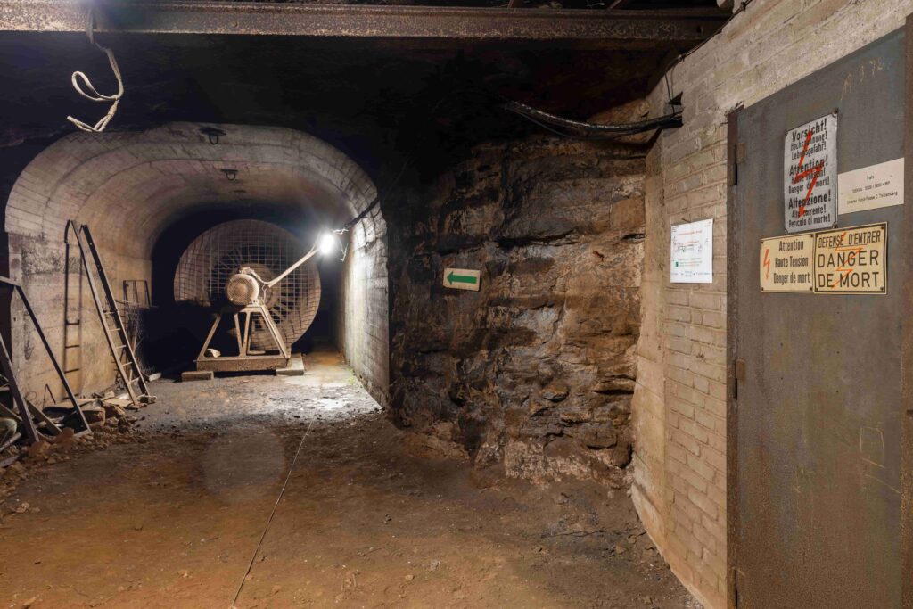 An illuminated mine ventilation fan inside an underground gallery with stone walls