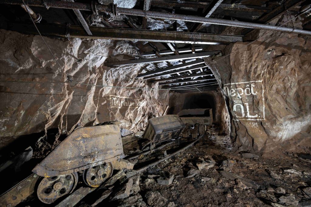 Rusty mining carts abandoned on rails inside a dark underground rock gallery