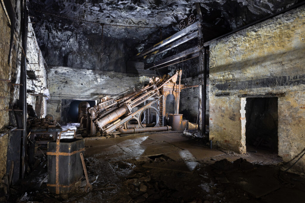 Une grande pompe industrielle rouillée installée dans une salle souterraine aux parois en pierre